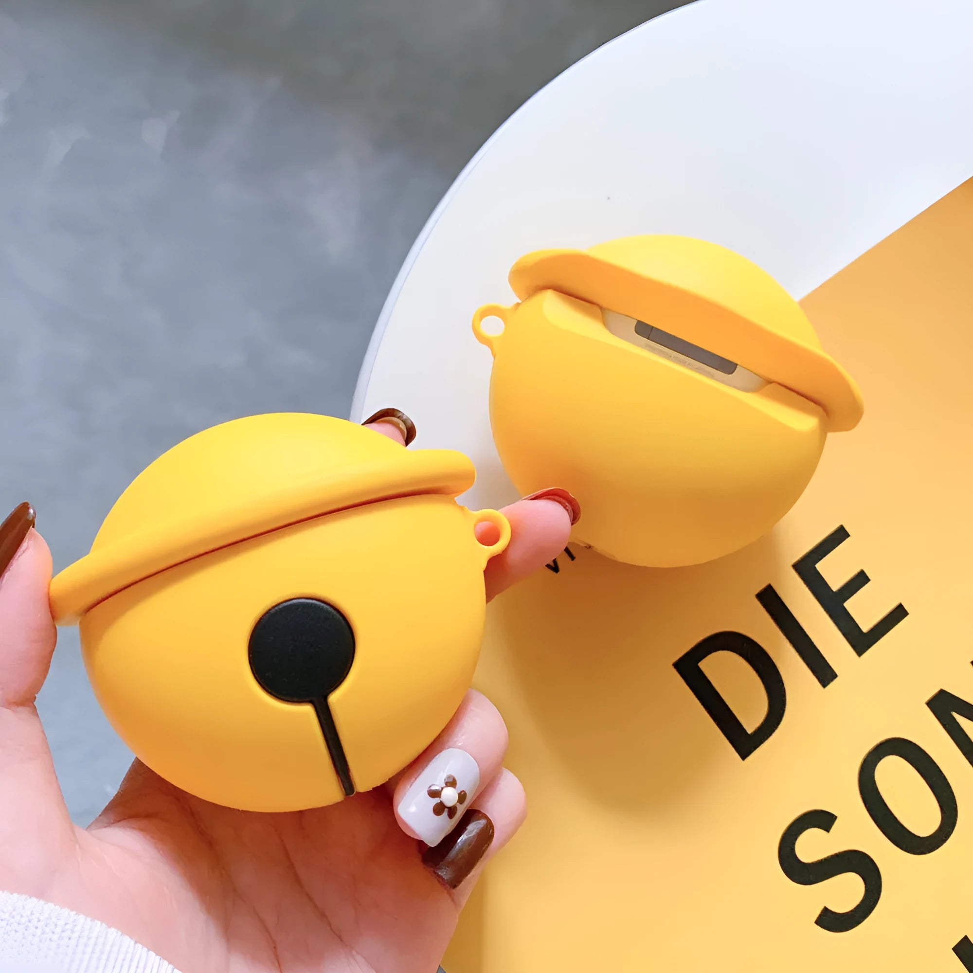 Bright yellow bell-shaped silicone protective case for Apple AirPods 1 and 2 with a carrying hook.