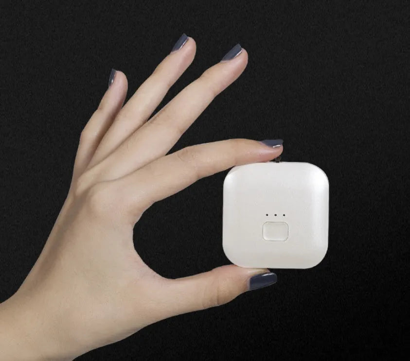 Small pink USB portable air purifier necklace on a table with charging cable.