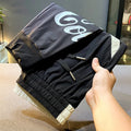 Black men's cropped casual trousers with an ankle-band cuff, laid flat to show the slim fit and cotton blend fabric.