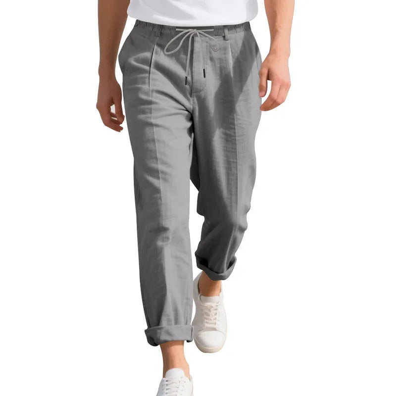 Men's straight leg linen trousers in light khaki colour with drawstring waist, laid flat.
