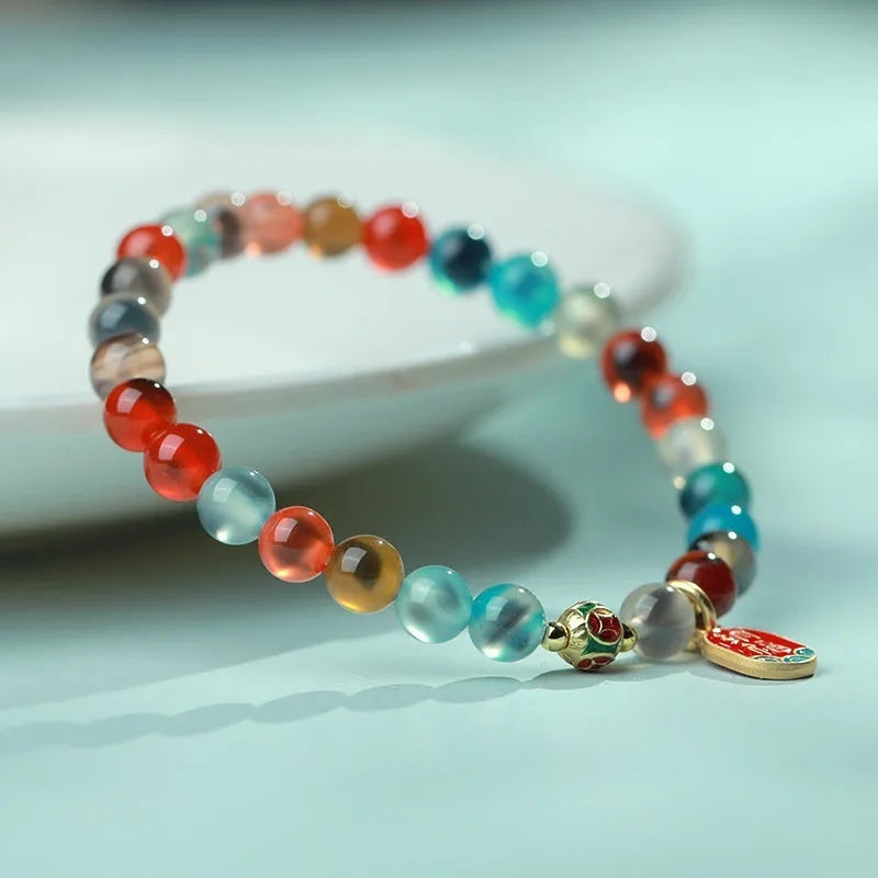 Close-up of a women's snake chain bracelet with colourful agate hearts and detailed copper coins.