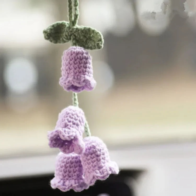 Green and white knitted wool car plant decoration with hanging rope on a car dashboard
