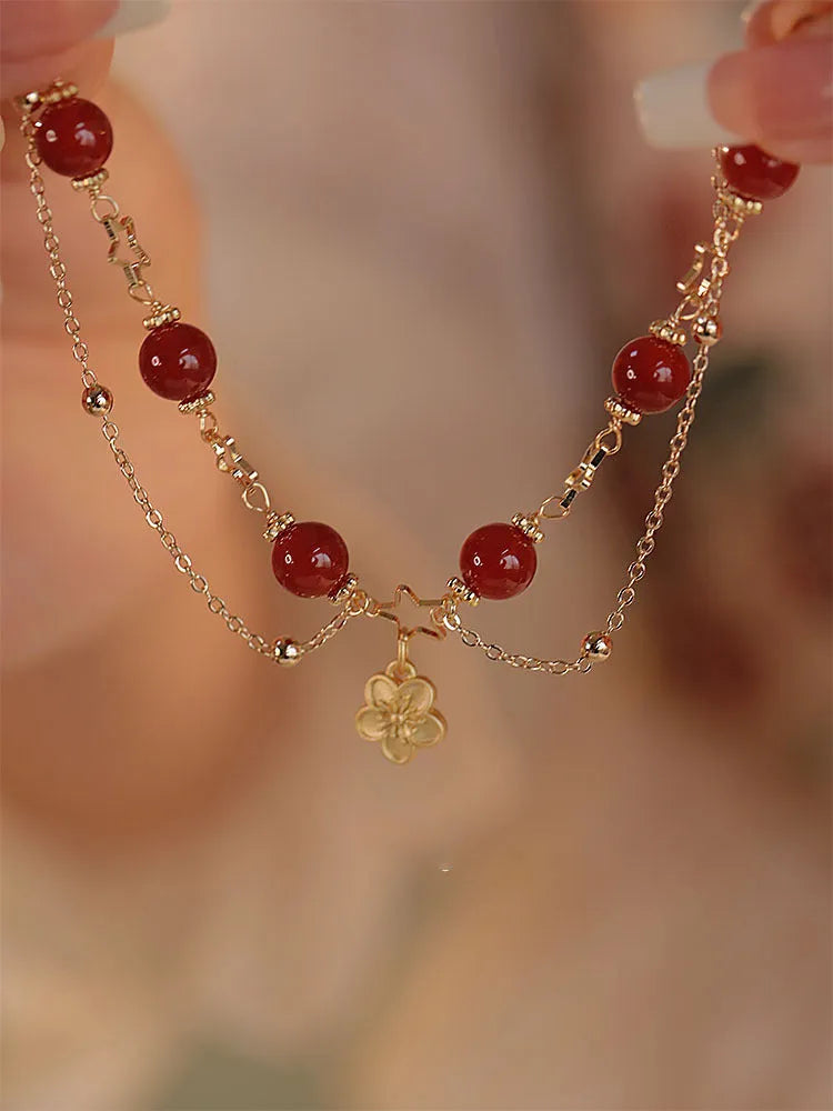 Red agate double layer bracelet with floral and peach blossom charms on a wrist.