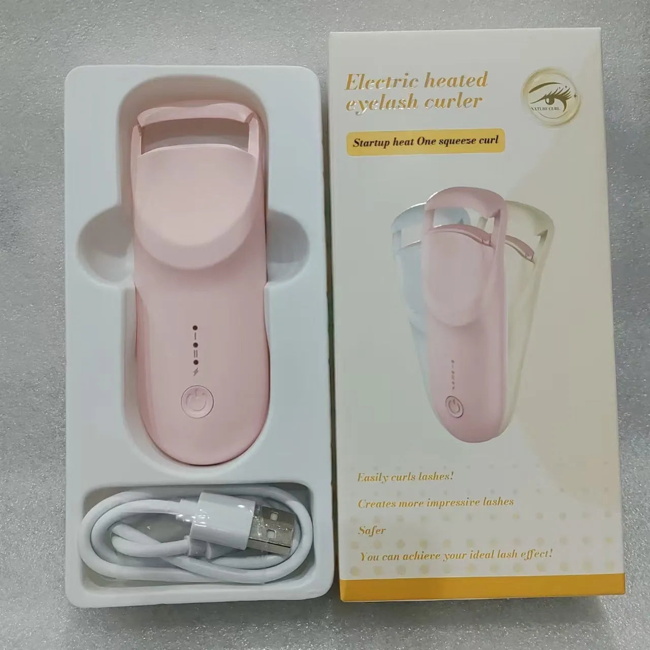 Electric heating eyelash curler in pink with USB charging cable on a white background