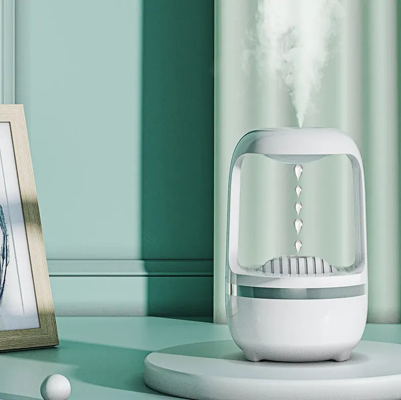 White anti-gravity humidifier on a desk showing water droplets in mid-air backflow, with USB cable.