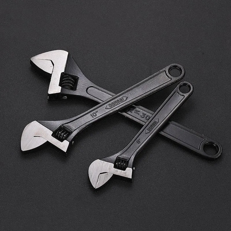 Black stainless steel adjustable open-end wrench on a workbench, showing size markings and ergonomic handle.