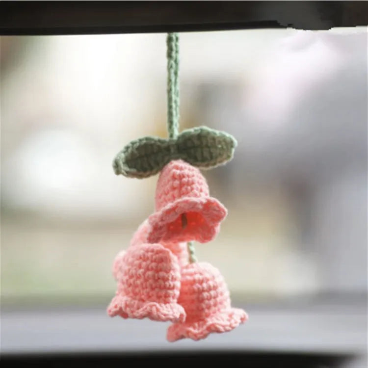 Green and white knitted wool car plant decoration with hanging rope on a car dashboard