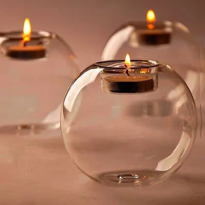 Handmade round hollow glass candle holder with openwork holes, shown on a table.