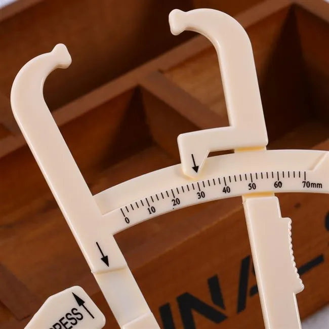 Clear acrylic body fat caliper showing measurement scales for skin fold thickness assessment