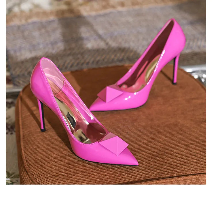 Women's pink patent leather pointed toe stiletto high heels with rivet and buckle decoration.