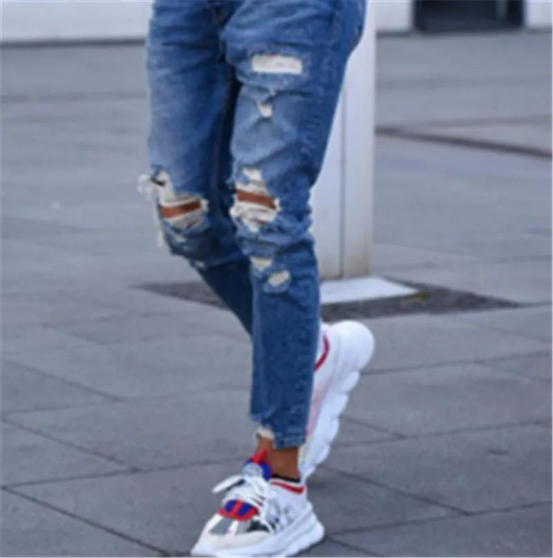 Men's deep blue cotton hole jeans laid flat, showing distressed detail and button fly.