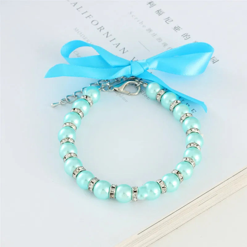 Small dog wearing adjustable blue imitation pearl and rhinestone necklace with ribbon bow