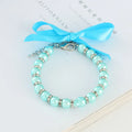 Small dog wearing adjustable blue imitation pearl and rhinestone necklace with ribbon bow