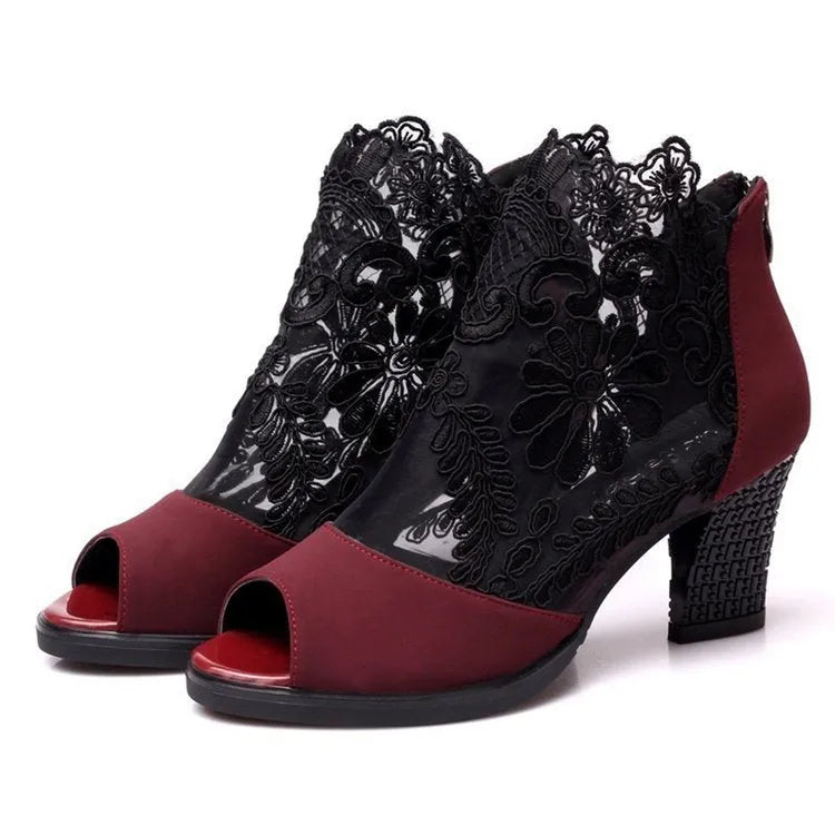 Black lace gladiator sandals with a flower motif, square high heel, and a front zip closure on a woman's foot.