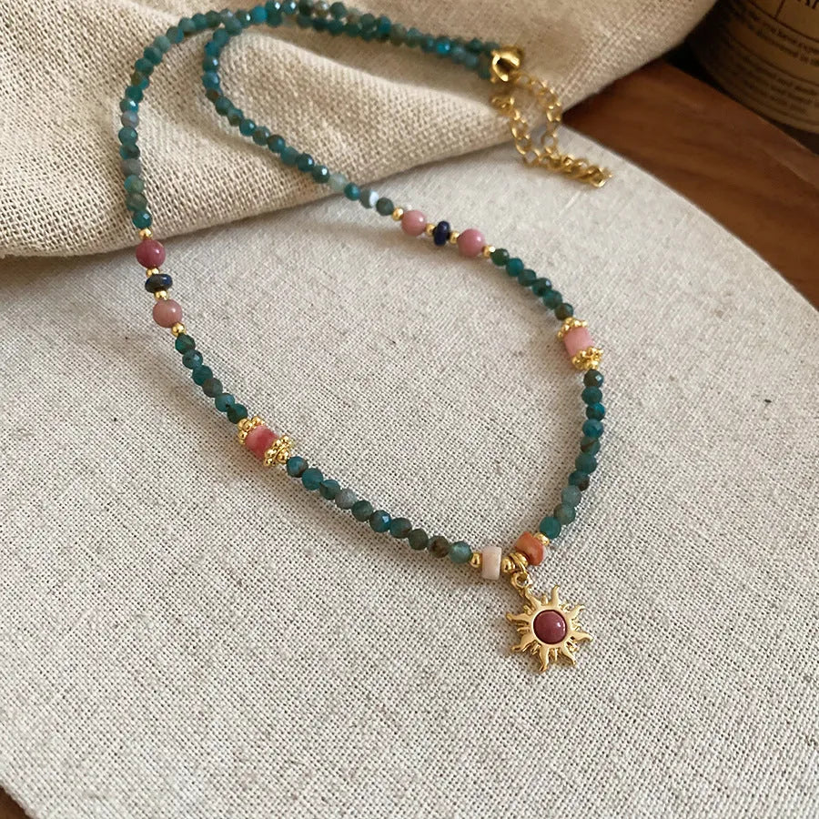 French royal style sun necklace with freshwater pearls and a blue stone geometry pendant on a gold chain.