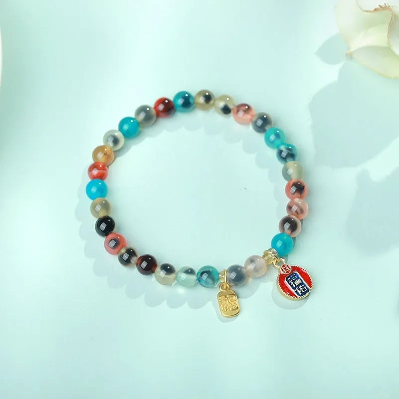 Close-up of a women's snake chain bracelet with colourful agate hearts and detailed copper coins.