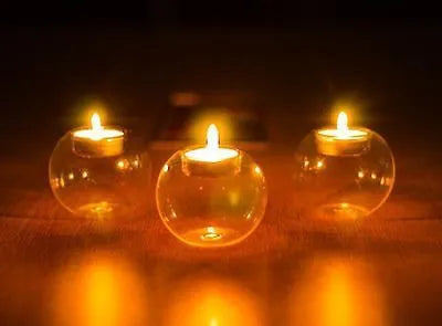 Handmade round hollow glass candle holder with openwork holes, shown on a table.