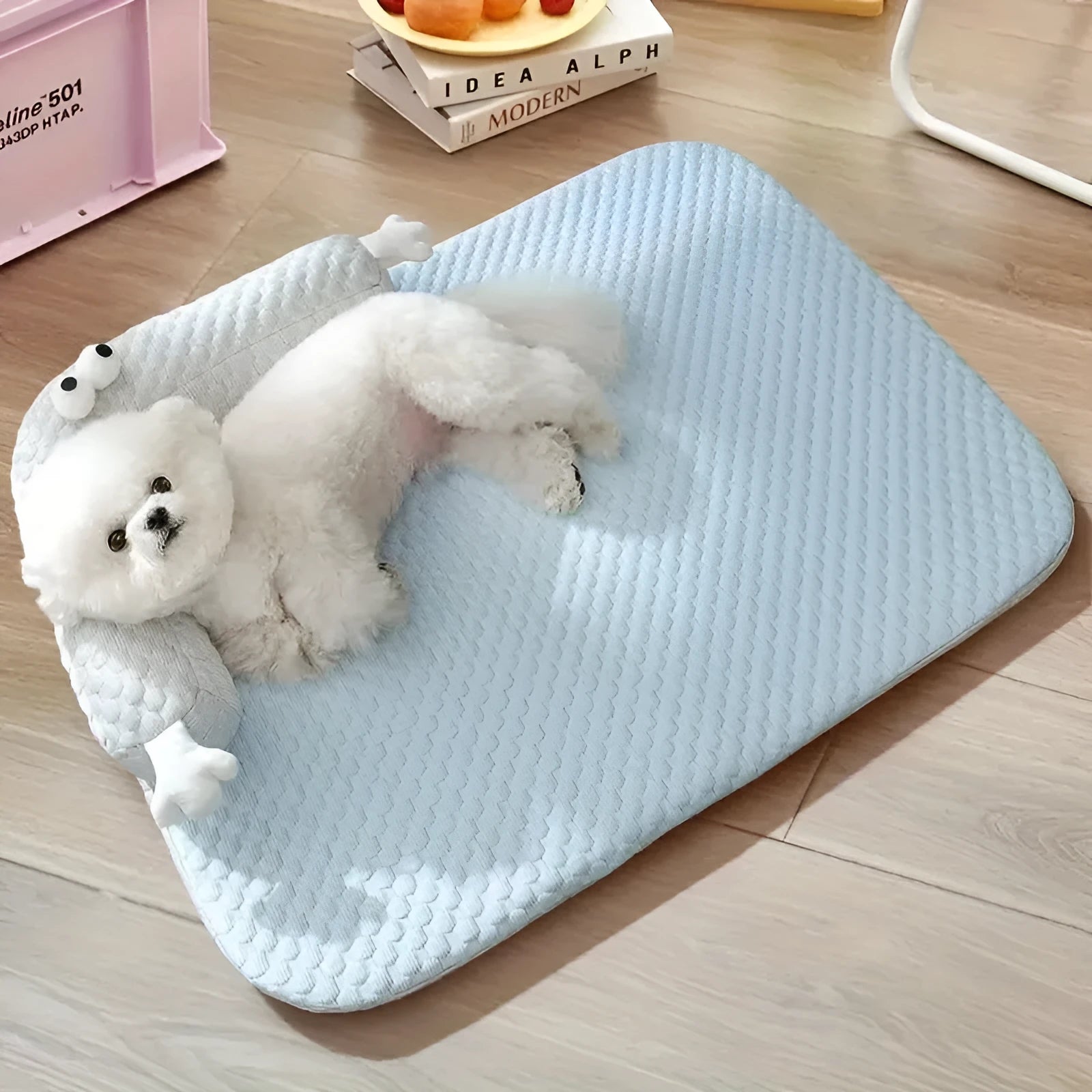 Blue polyester pet bed cushion with printed big-eyed monster face design, shown on a wooden floor.