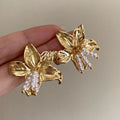 A pair of exaggerated gold metal flower earrings with pearl centres, showing a niche floral jewellery design.