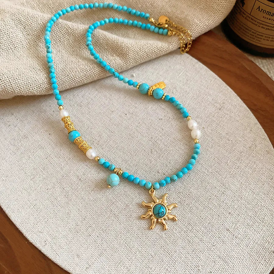 French royal style sun necklace with freshwater pearls and a blue stone geometry pendant on a gold chain.