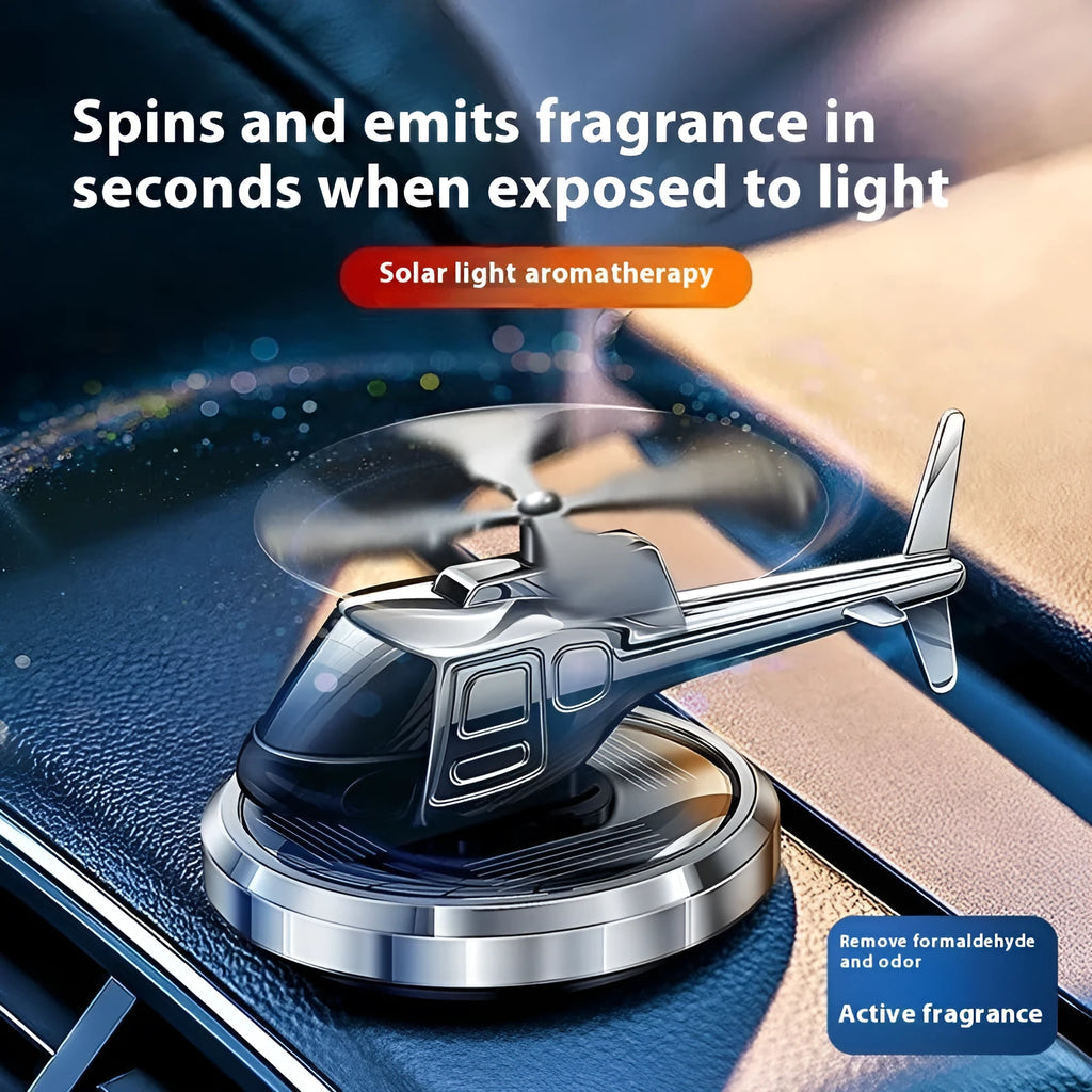 Silver metal solar helicopter car air freshener ornament with rotating blades on a car dashboard.