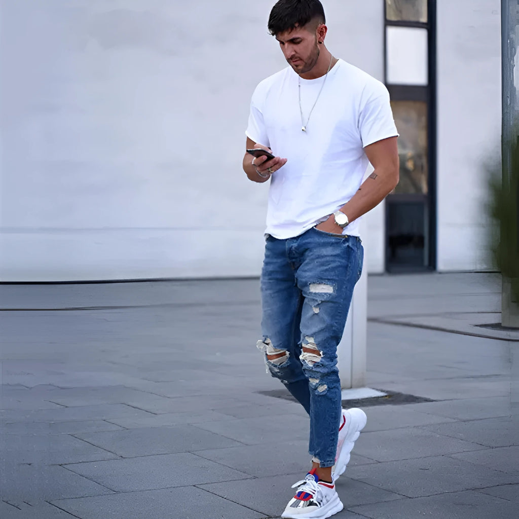 Men's deep blue cotton hole jeans laid flat, showing distressed detail and button fly.