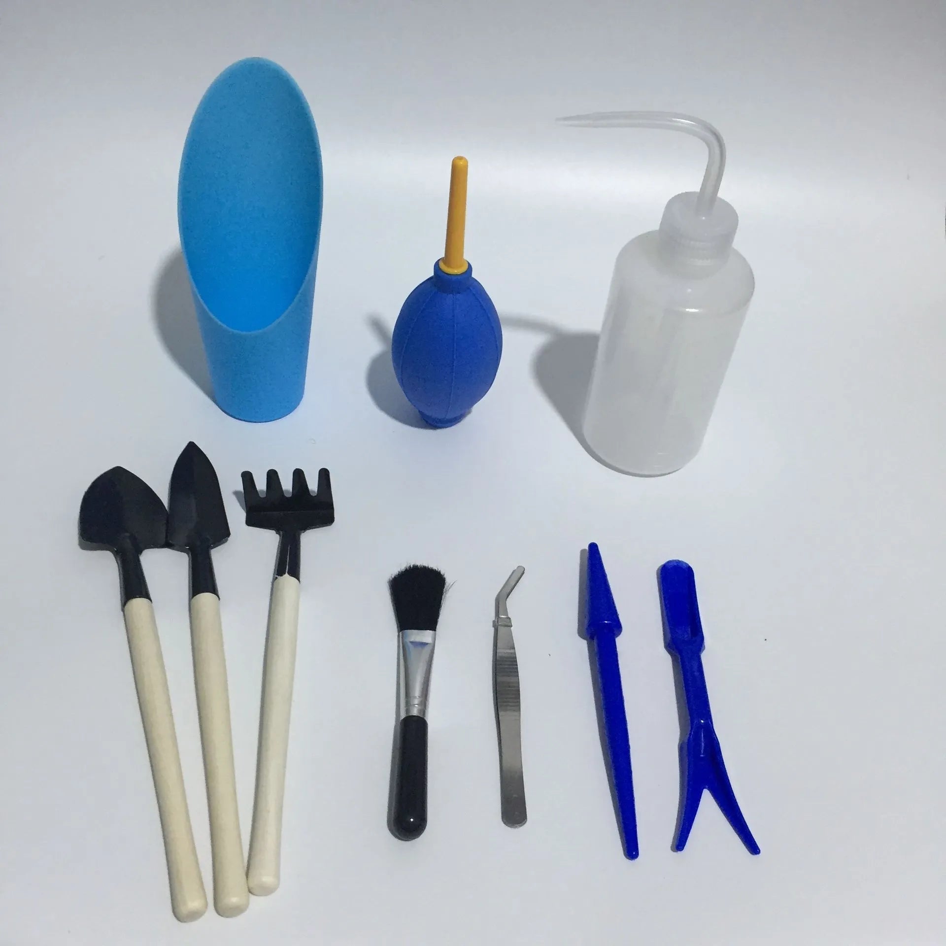 Succulent gardening tool set with plastic watering can, mini shovel, tweezers, and small brush arranged for indoor plant care
