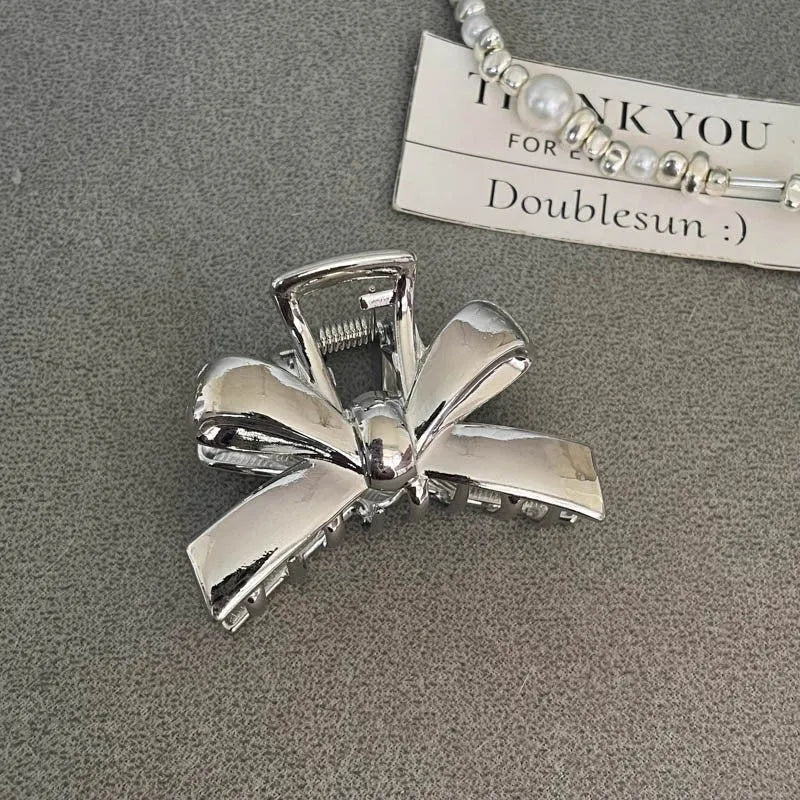 Silver metal hair claw clip assortment showing bows, waves, pearl designs, and geometric shapes from 4cm to 13.5cm