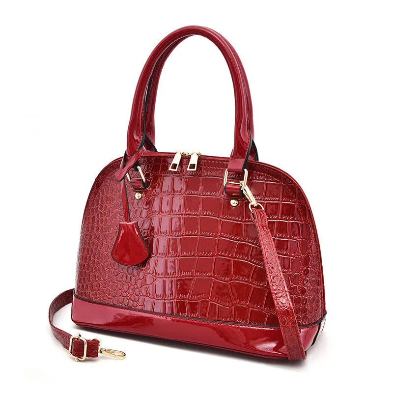 Large shiny PU crossbody shoulder bag in structured shell shape showing black, red, and brown colour options
