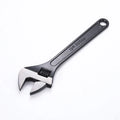 Black stainless steel adjustable open-end wrench on a workbench, showing size markings and ergonomic handle.