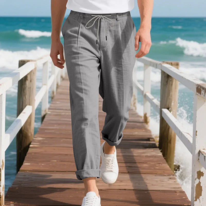 Men's straight leg linen trousers in light khaki colour with drawstring waist, laid flat.
