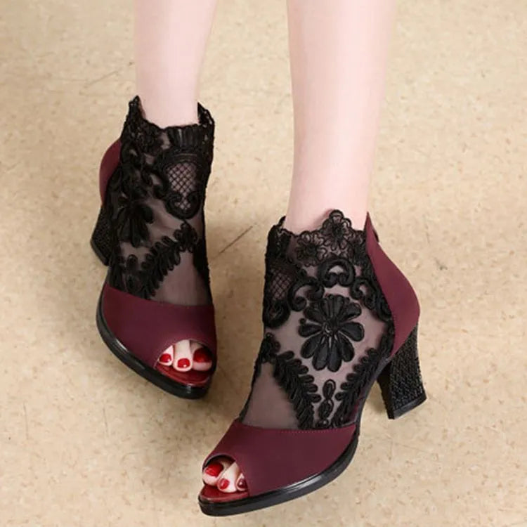 Black lace gladiator sandals with a flower motif, square high heel, and a front zip closure on a woman's foot.