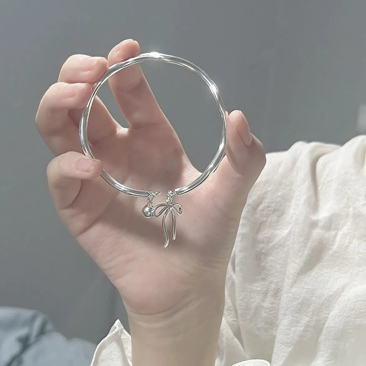 Silver adjustable bracelet with a bow charm and a visible bell-opening clasp on a white background.