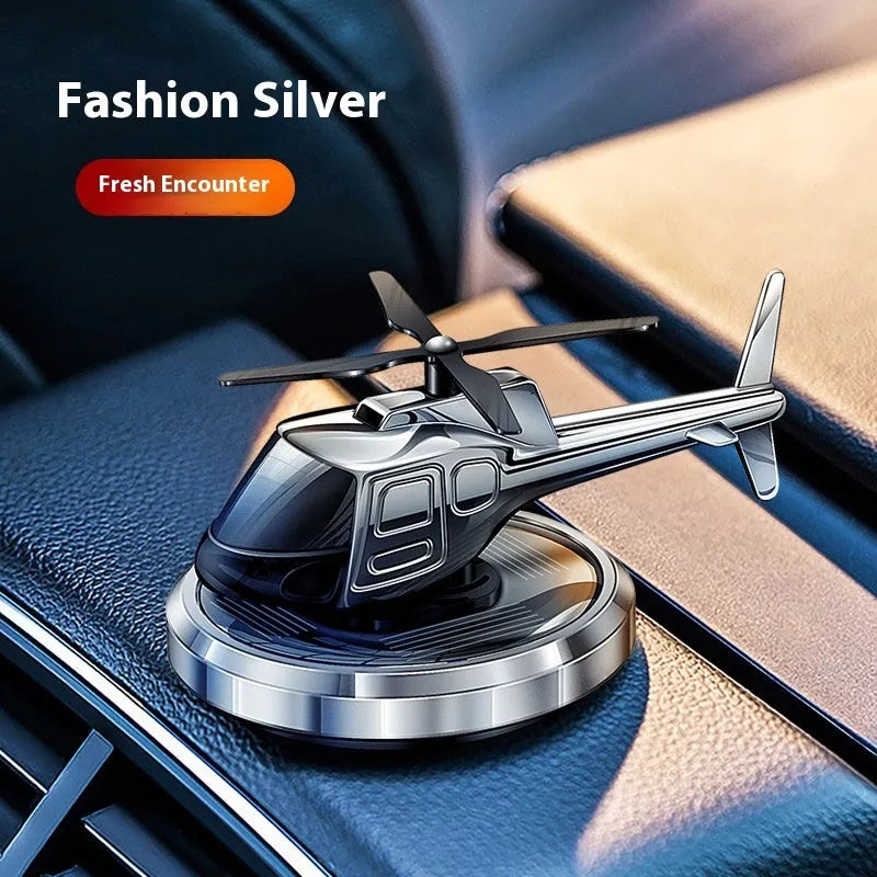 Silver metal solar helicopter car air freshener ornament with rotating blades on a car dashboard.