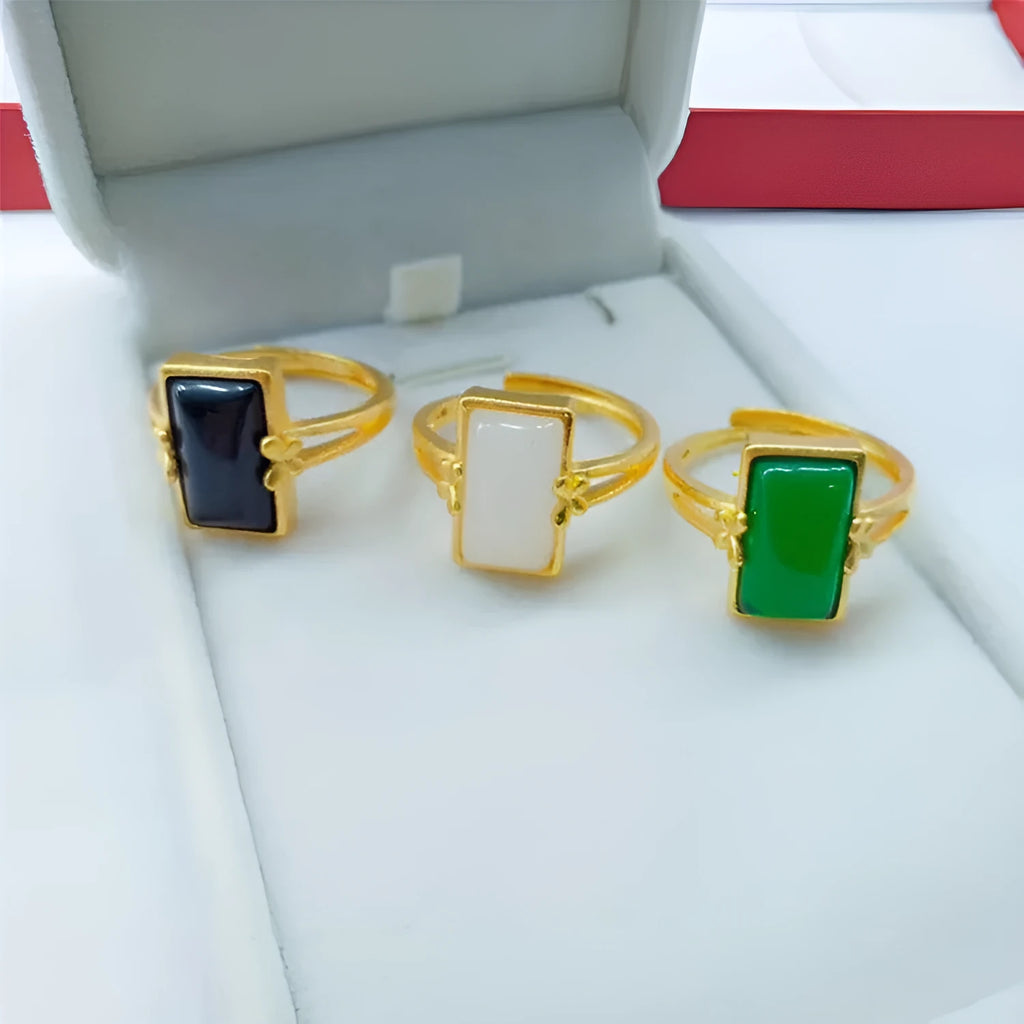 Adjustable brass gold-plated ring with a central green gemstone on a model's hand.