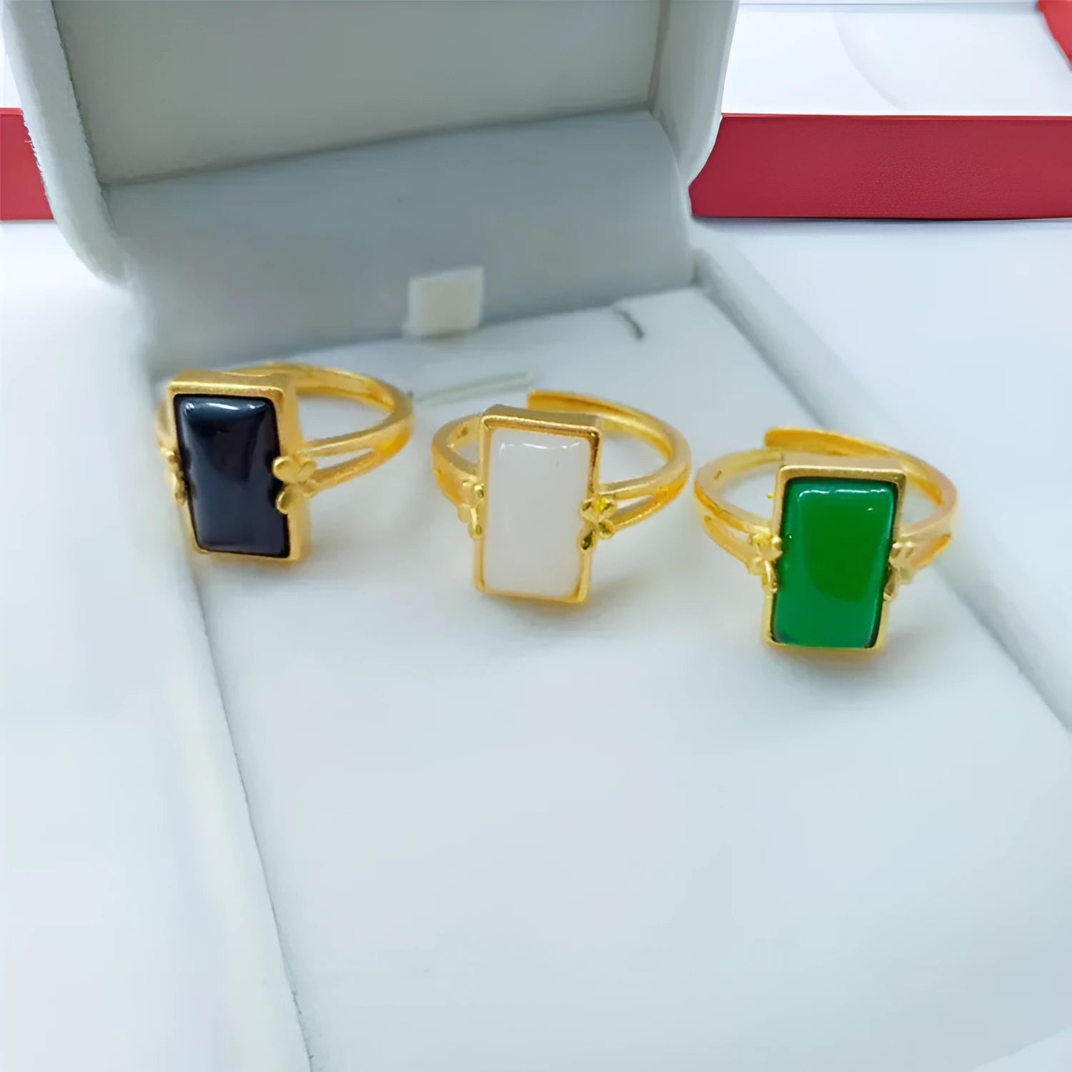 Adjustable brass gold-plated ring with a central green gemstone on a model's hand.