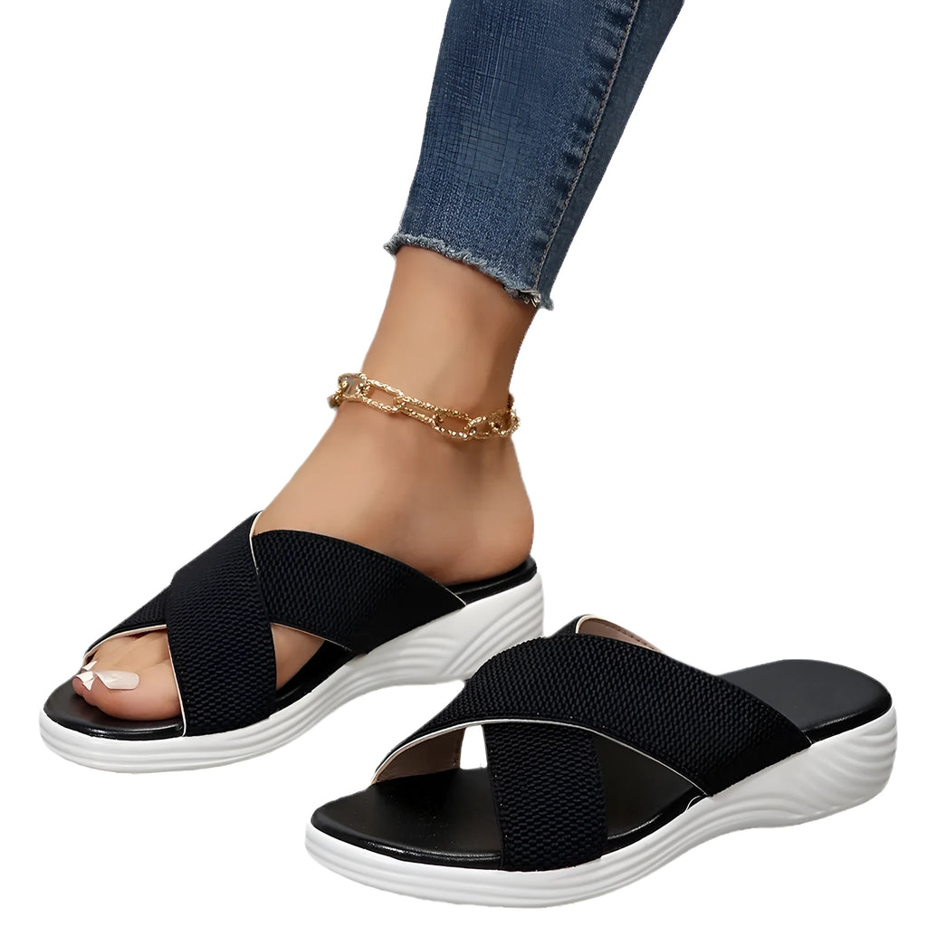 Black wedge platform slippers with a cross strap and open peep-toe design on a white background.