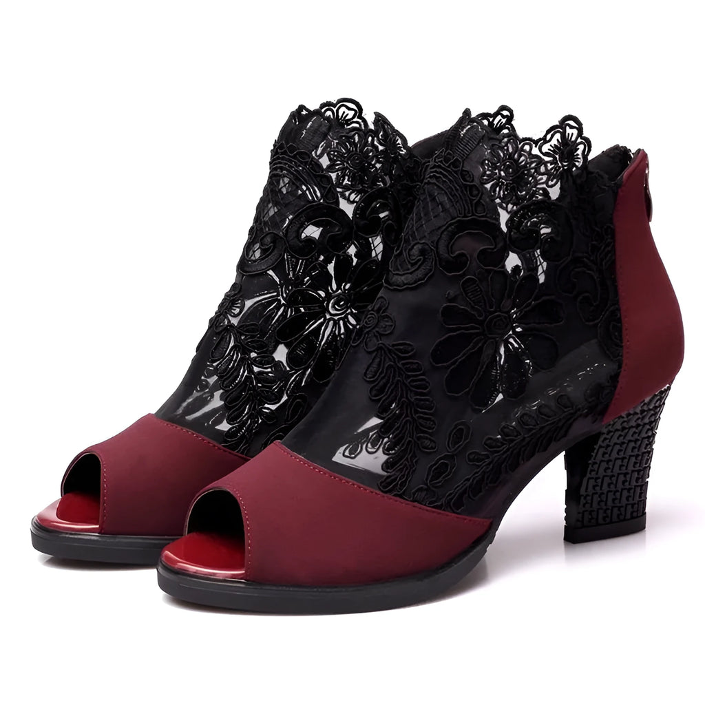 Black lace gladiator sandals with a flower motif, square high heel, and a front zip closure on a woman's foot.