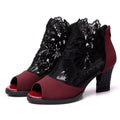 Black lace gladiator sandals with a flower motif, square high heel, and a front zip closure on a woman's foot.