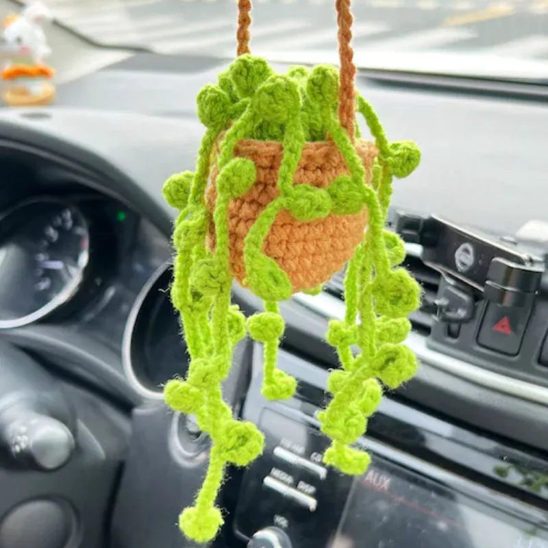 Green and white knitted wool car plant decoration with hanging rope on a car dashboard
