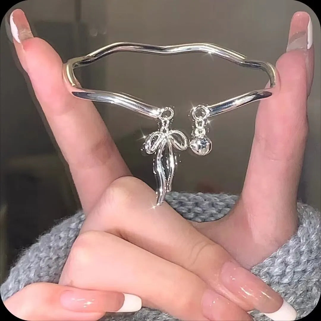 Silver adjustable bracelet with a bow charm and a visible bell-opening clasp on a white background.
