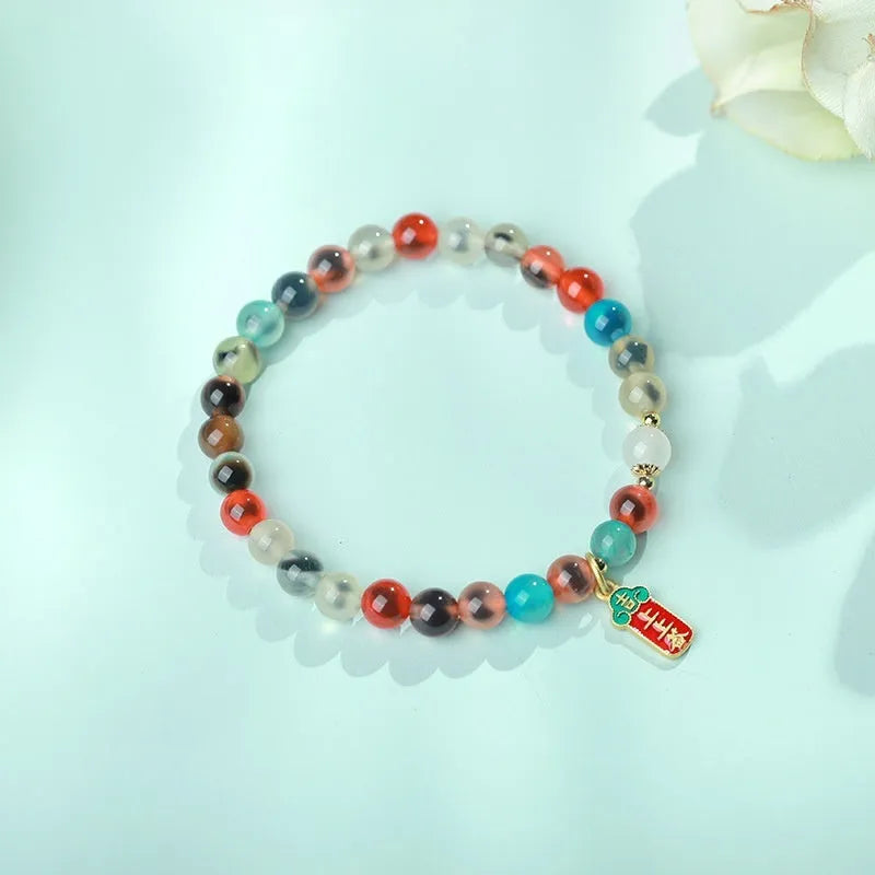 Close-up of a women's snake chain bracelet with colourful agate hearts and detailed copper coins.
