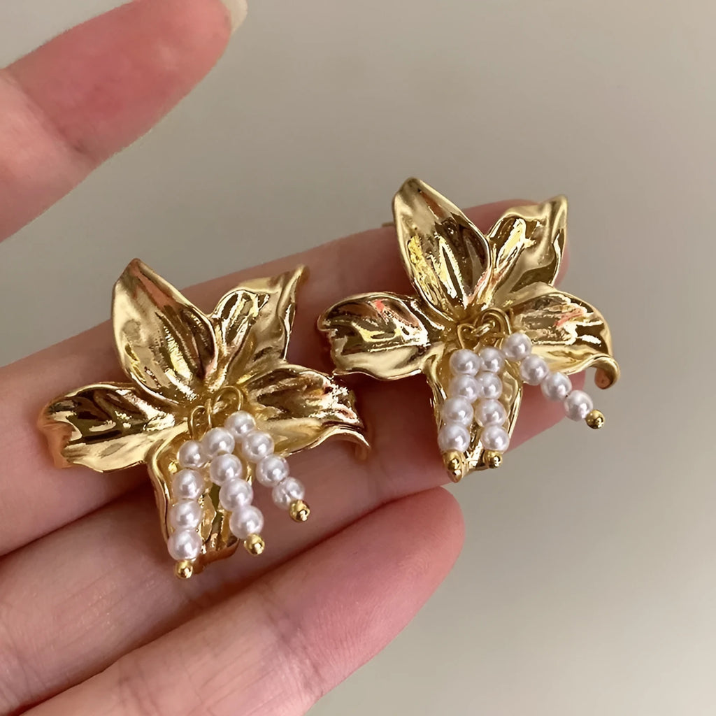 A pair of exaggerated gold metal flower earrings with pearl centres, showing a niche floral jewellery design.
