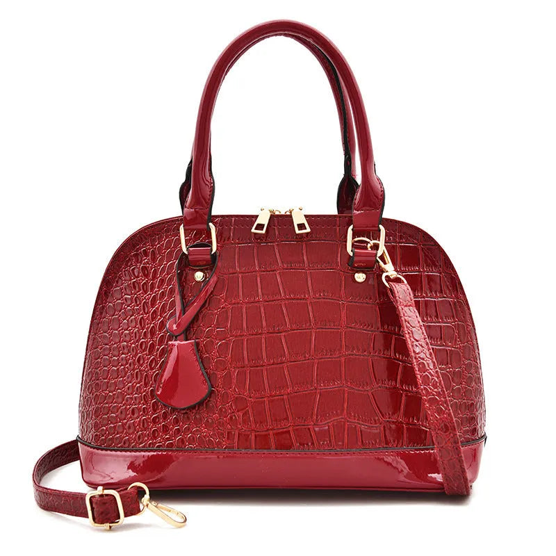 Large shiny PU crossbody shoulder bag in structured shell shape showing black, red, and brown colour options