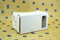 Pink and white folding cardboard VR glasses viewer for smartphones with 3D lenses and head strap.