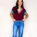 Burgundy loose sweater with V-neck, contrast trim, and cuffed short sleeves on a hanger.