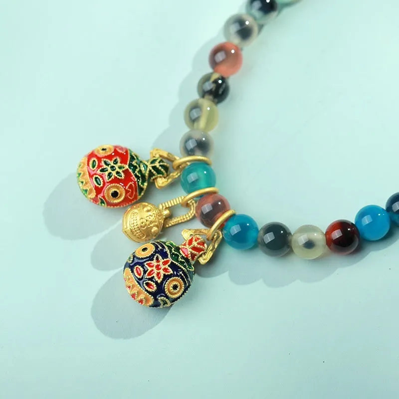 Close-up of a women's snake chain bracelet with colourful agate hearts and detailed copper coins.