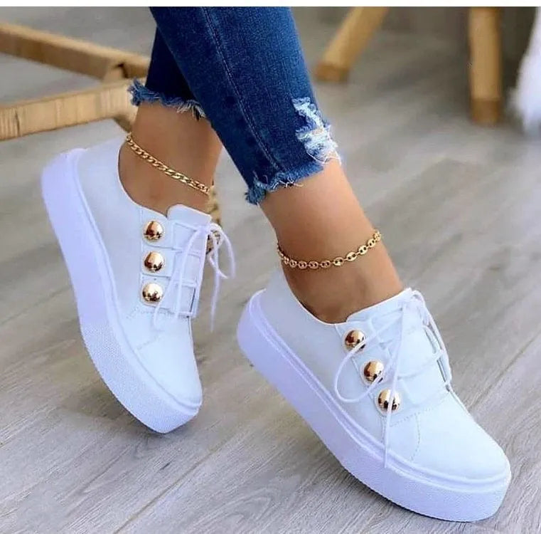 Women's white lace-up flat sneakers with silver rivet detailing on a round toe.
