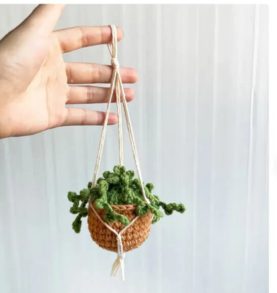Green and white knitted wool car plant decoration with hanging rope on a car dashboard