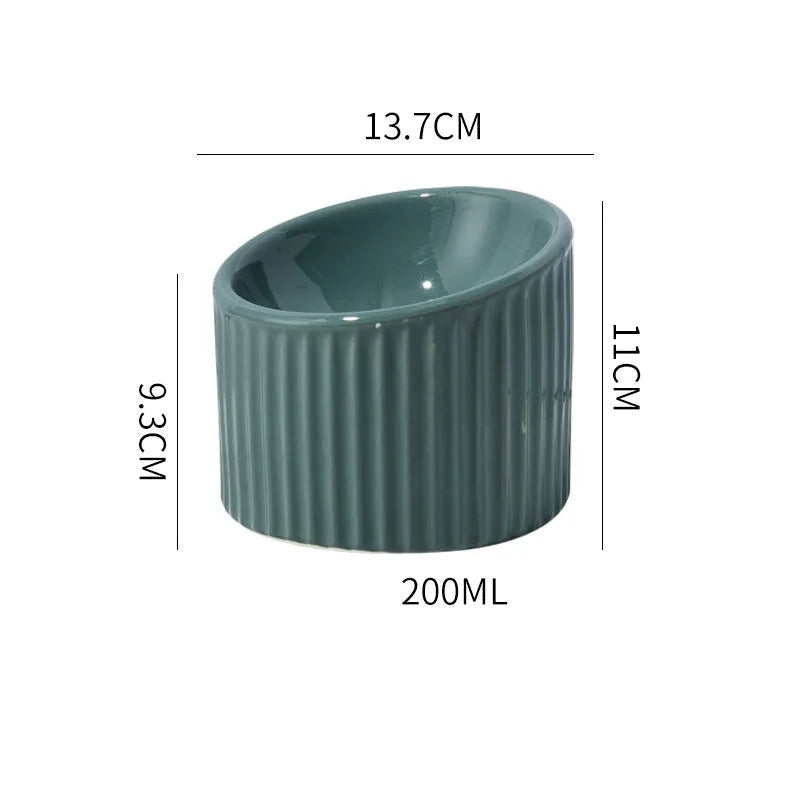 Dark green ceramic elevated cat bowl with tilted, round whisker-friendly design on a wooden floor.